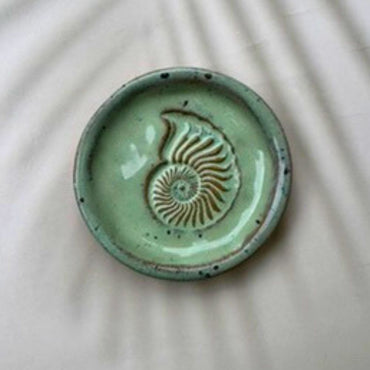 Green ceramic dish with a shell design on a beige background