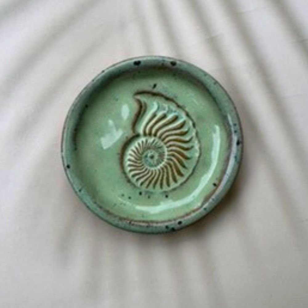Green ceramic dish with a shell design on a beige background