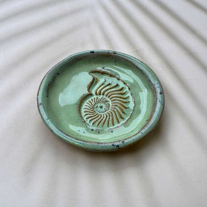 Green ceramic dish with shell design on a beige surface