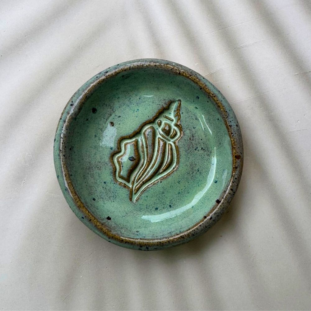 Green ceramic dish with a shell design on a textured surface