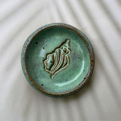 Green ceramic dish with a shell design on a textured surface