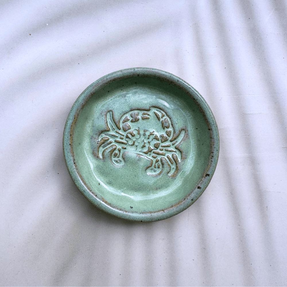 Green ceramic dish with a crab design on a white fabric background