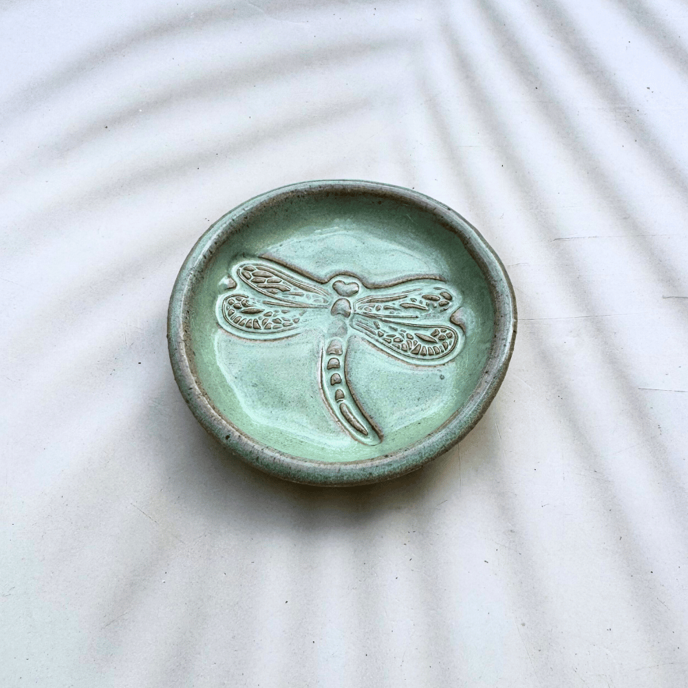 Green ceramic dish with a dragonfly design on a textured white surface
