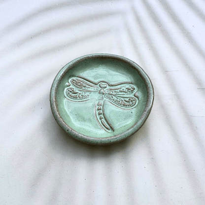 Green ceramic dish with a dragonfly design on a textured white surface