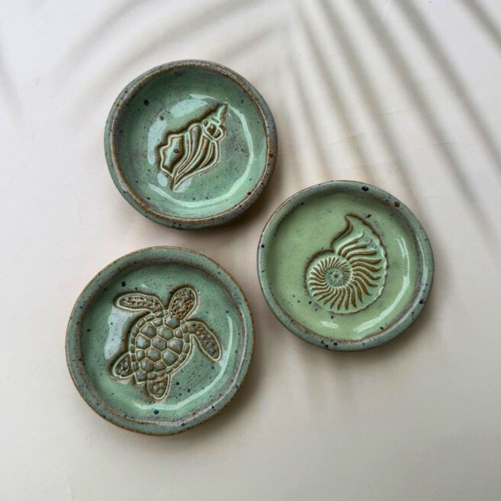 Three ceramic plates with embossed designs of a shell, turtle, and ammonite on a beige background.