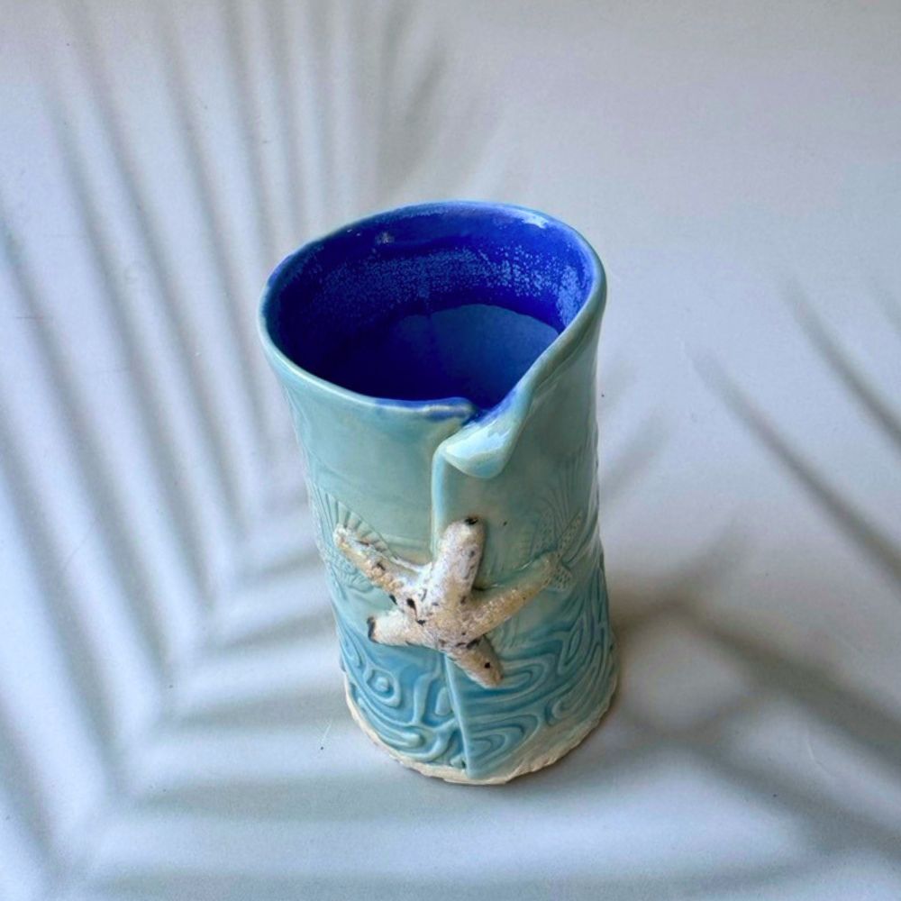Blue ceramic bud vase with starfish design on a textured white surface