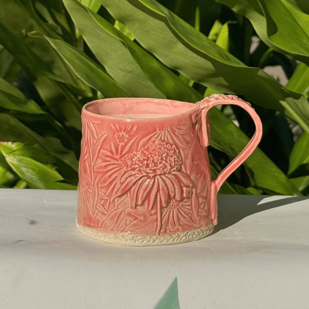 Ceramic mug with floral design on a white surface with green leaves in the background