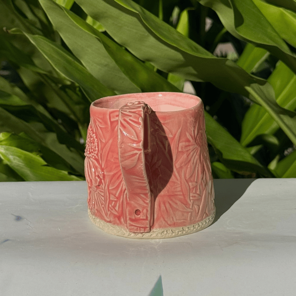 Pink ceramic vase with textured design on a white surface with green leaves in the background
