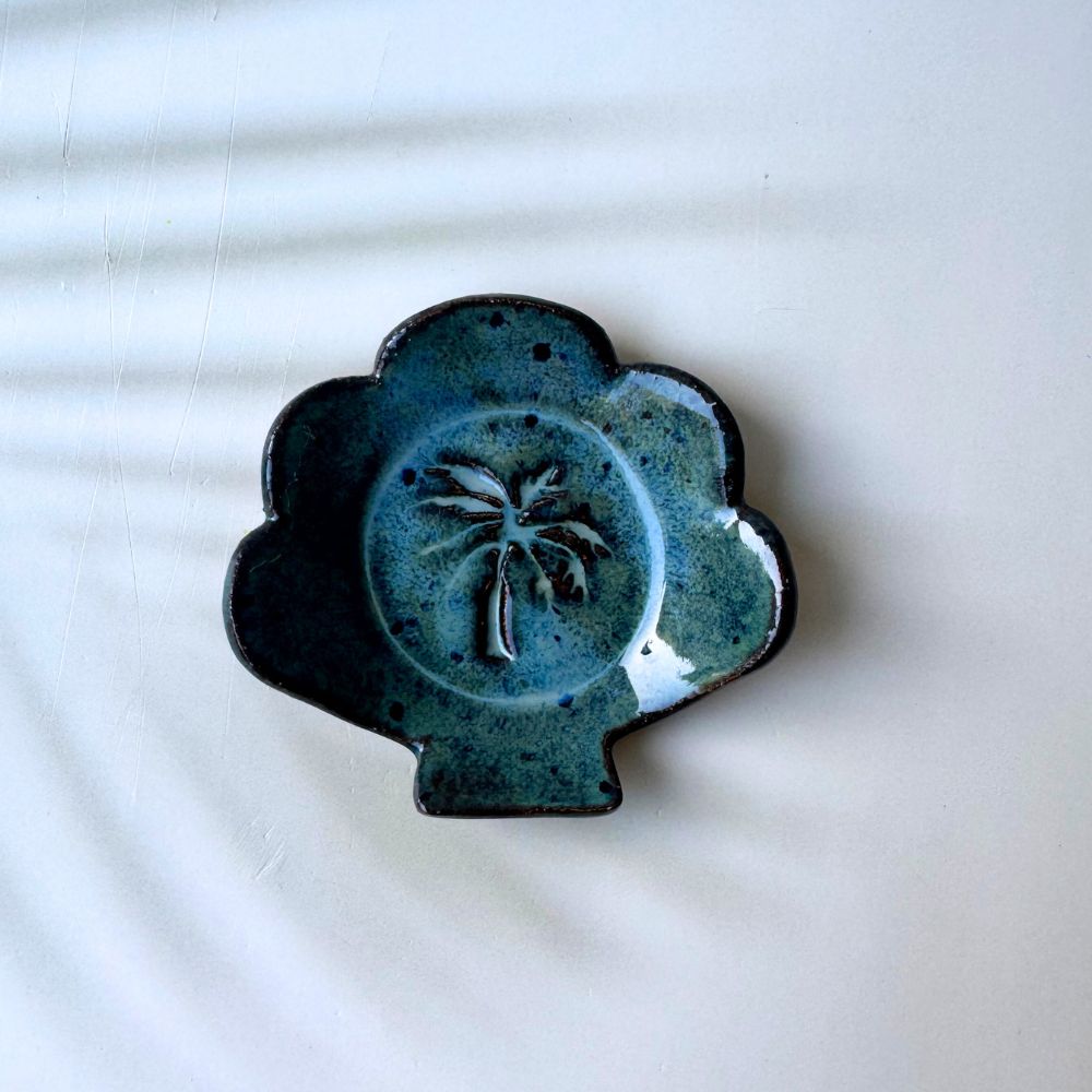 Blue ceramic ring dish shell shaped with a palm tree design on a white background