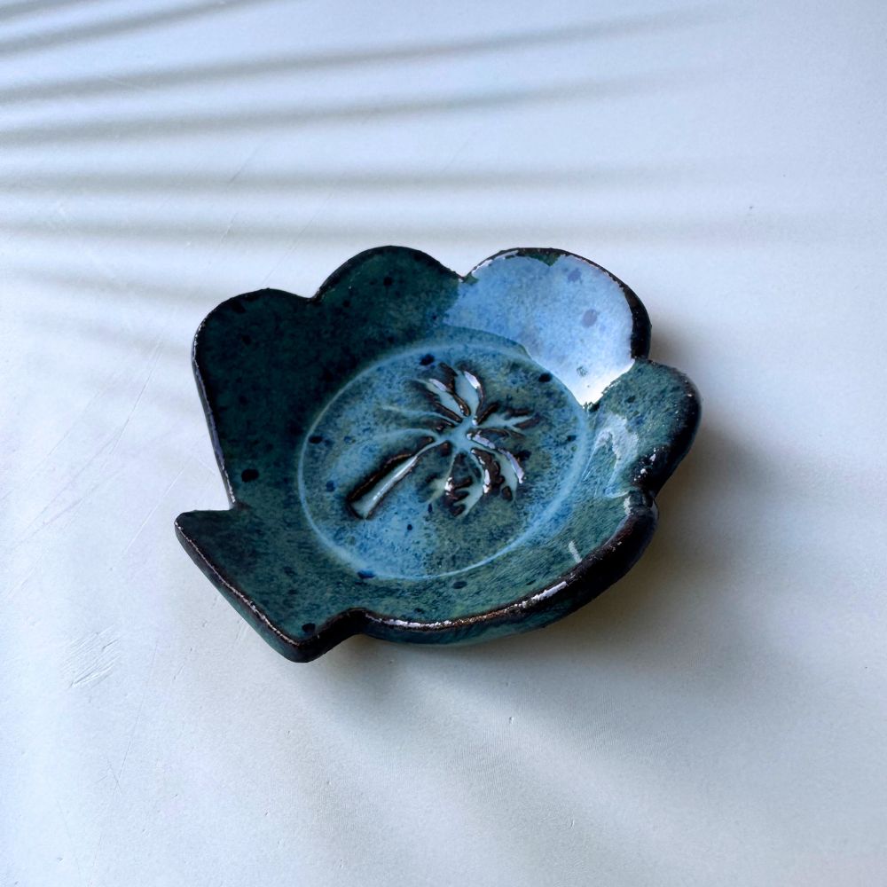 Blue ceramic ring dish shell shaped with a palm tree design on a white background