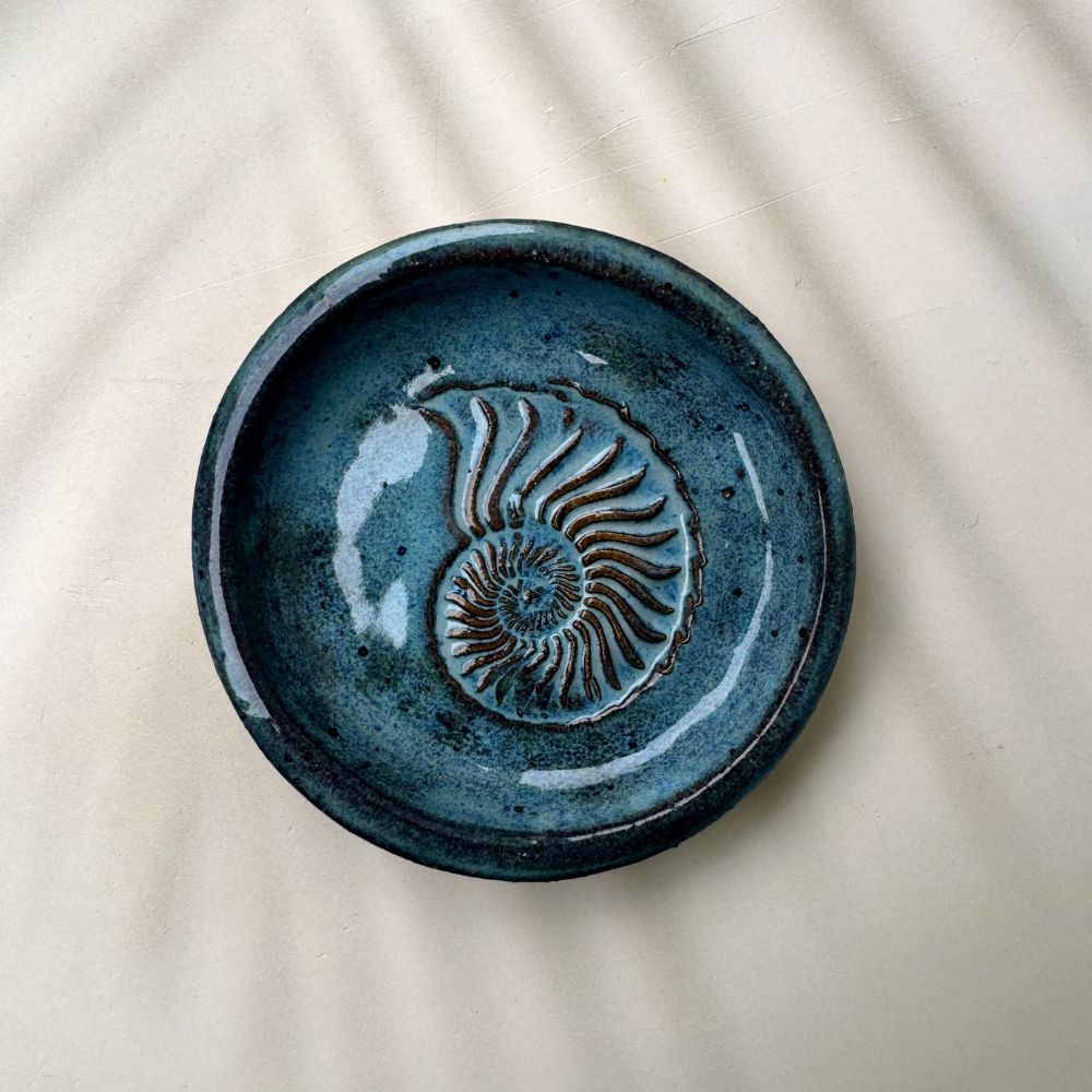 Blue ceramic ring dish with a shell design on a beige fabric background