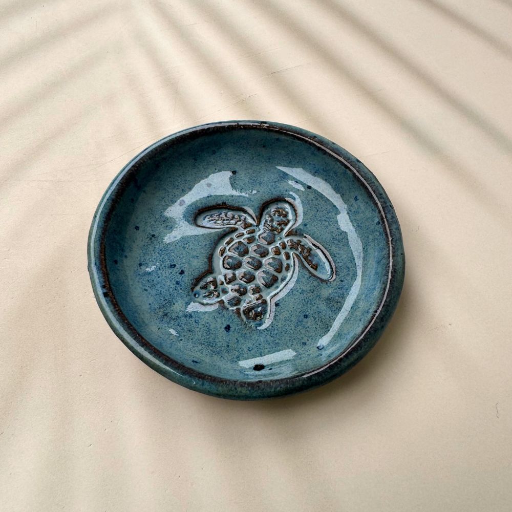 Blue ceramic ring dish with a turtle design on a beige surface