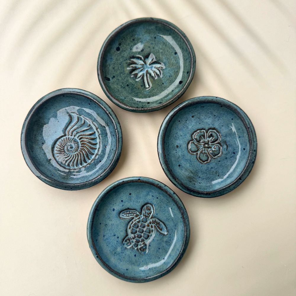 Four blue ceramic trinket dishes with embossed designs on a beige background