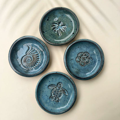 Four blue ceramic trinket dishes with embossed designs on a beige background