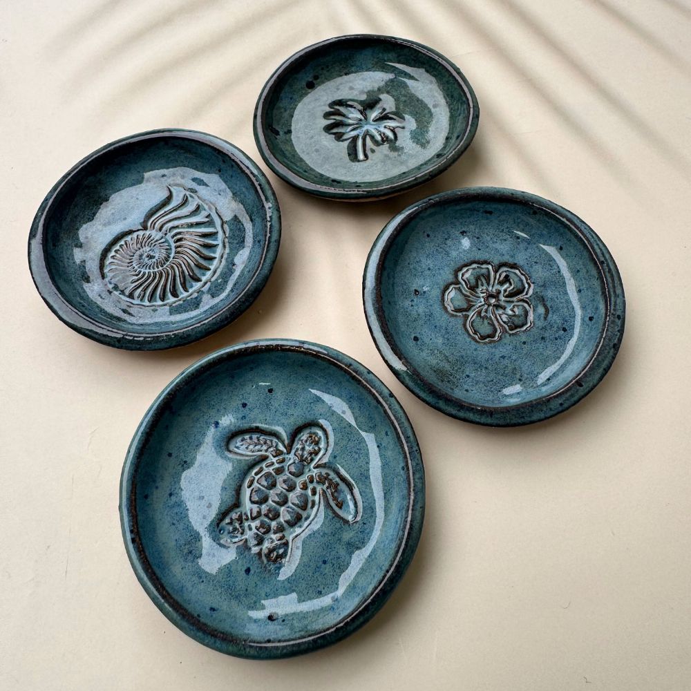 Four blue ceramic trinket dishes with embossed designs on a beige surface