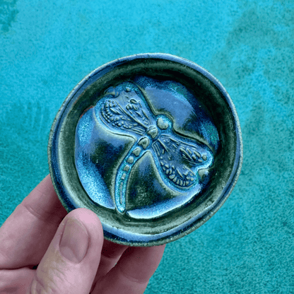 Ceramic ring dish with a dragonfly design held against a teal background