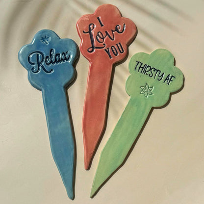 Three decorative garden sticks with text on a beige background