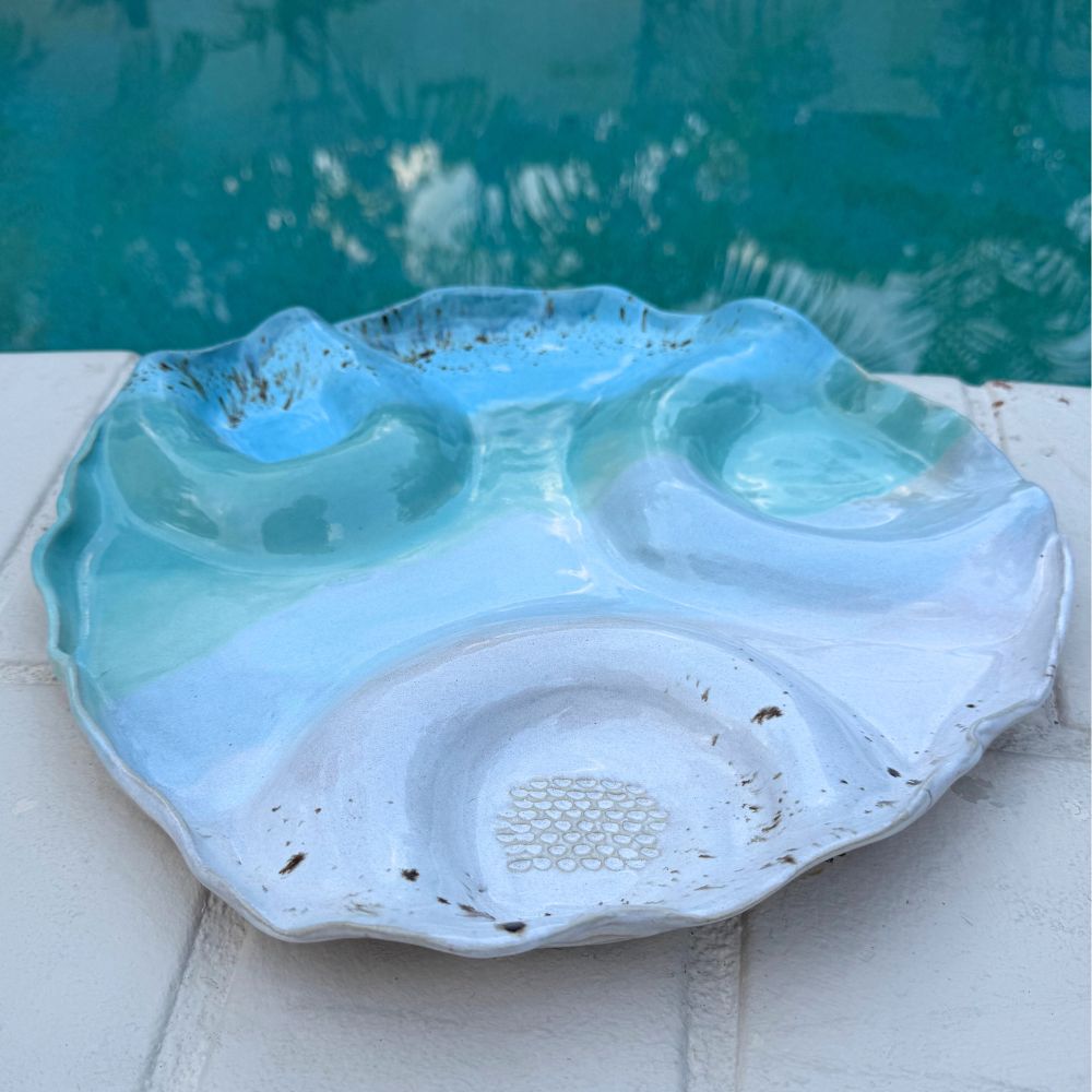 Large shell dish with a textured surface on a white ledge by a pool.
