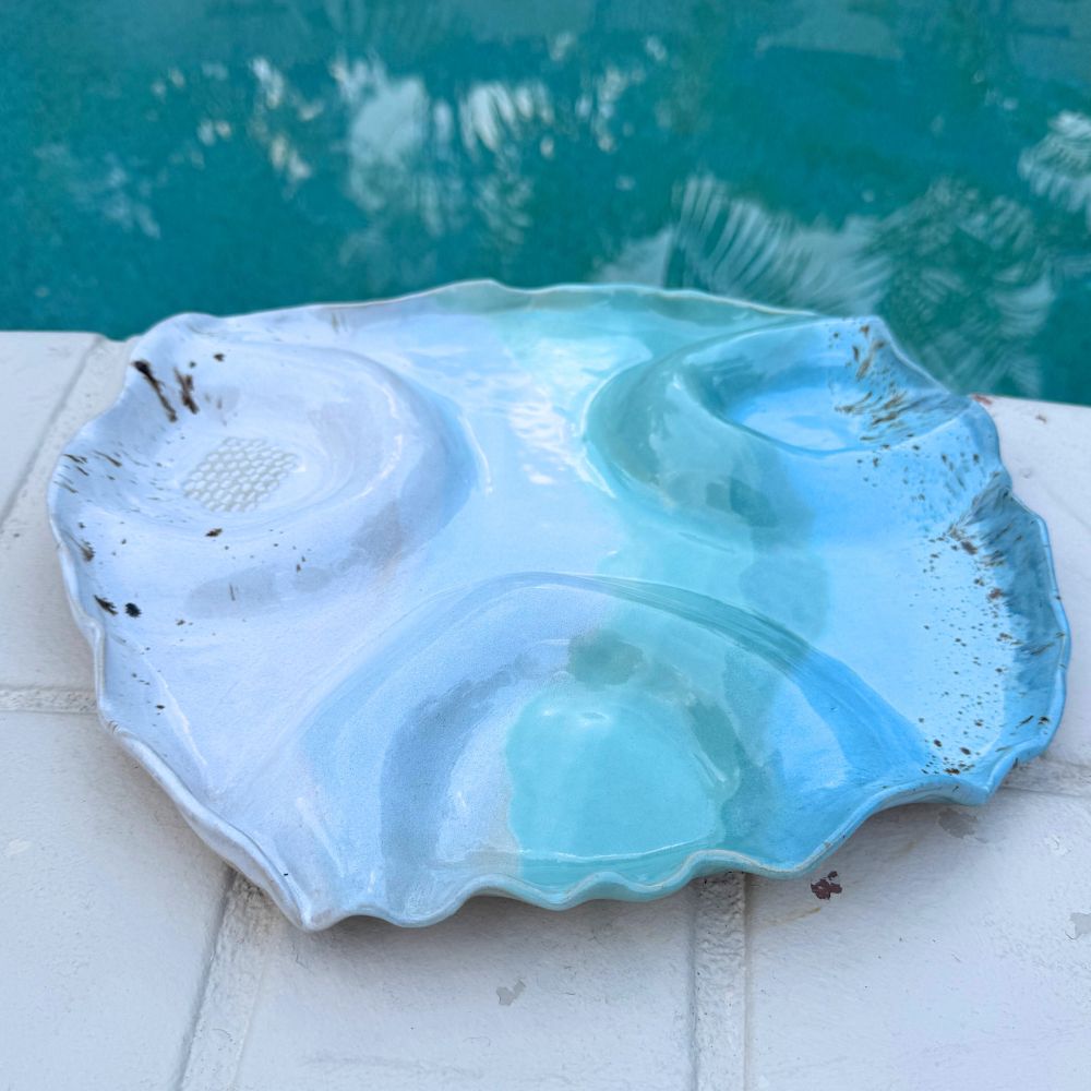 Blue ceramic shell-shaped dish on a white surface with a pool in the background