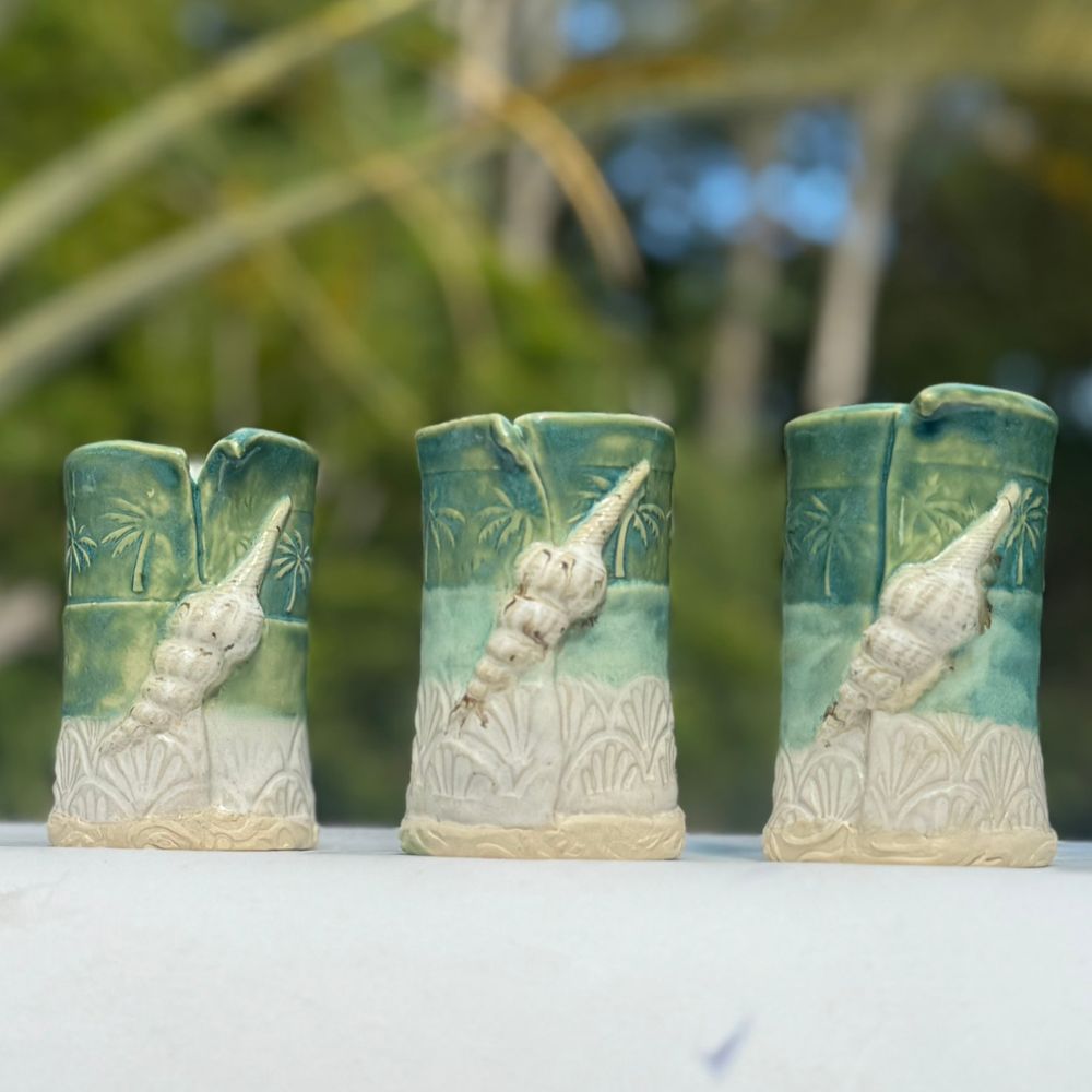 Three ceramic vases with shell designs on a white surface with a blurred natural background
