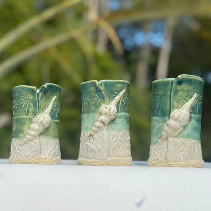 Three ceramic vases with shell designs on a white surface with a blurred natural background