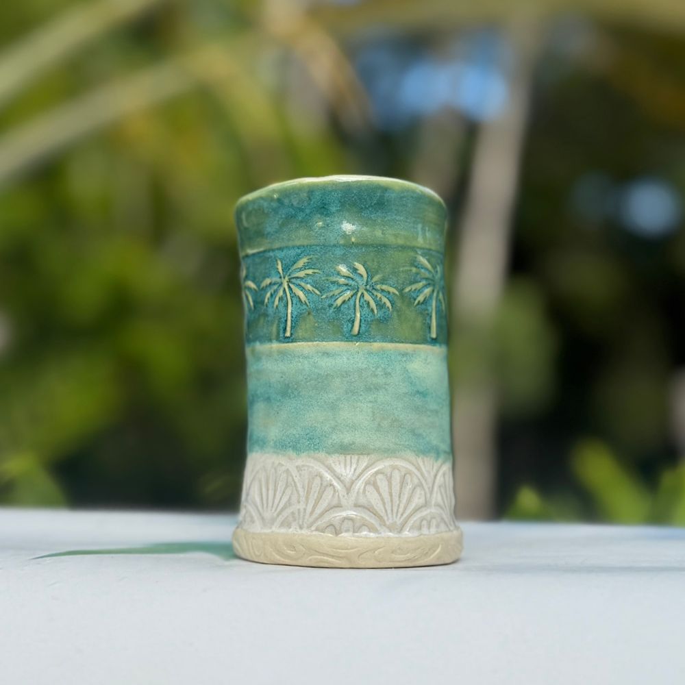 Green ceramic vase with decorative patterns on a blurred natural background