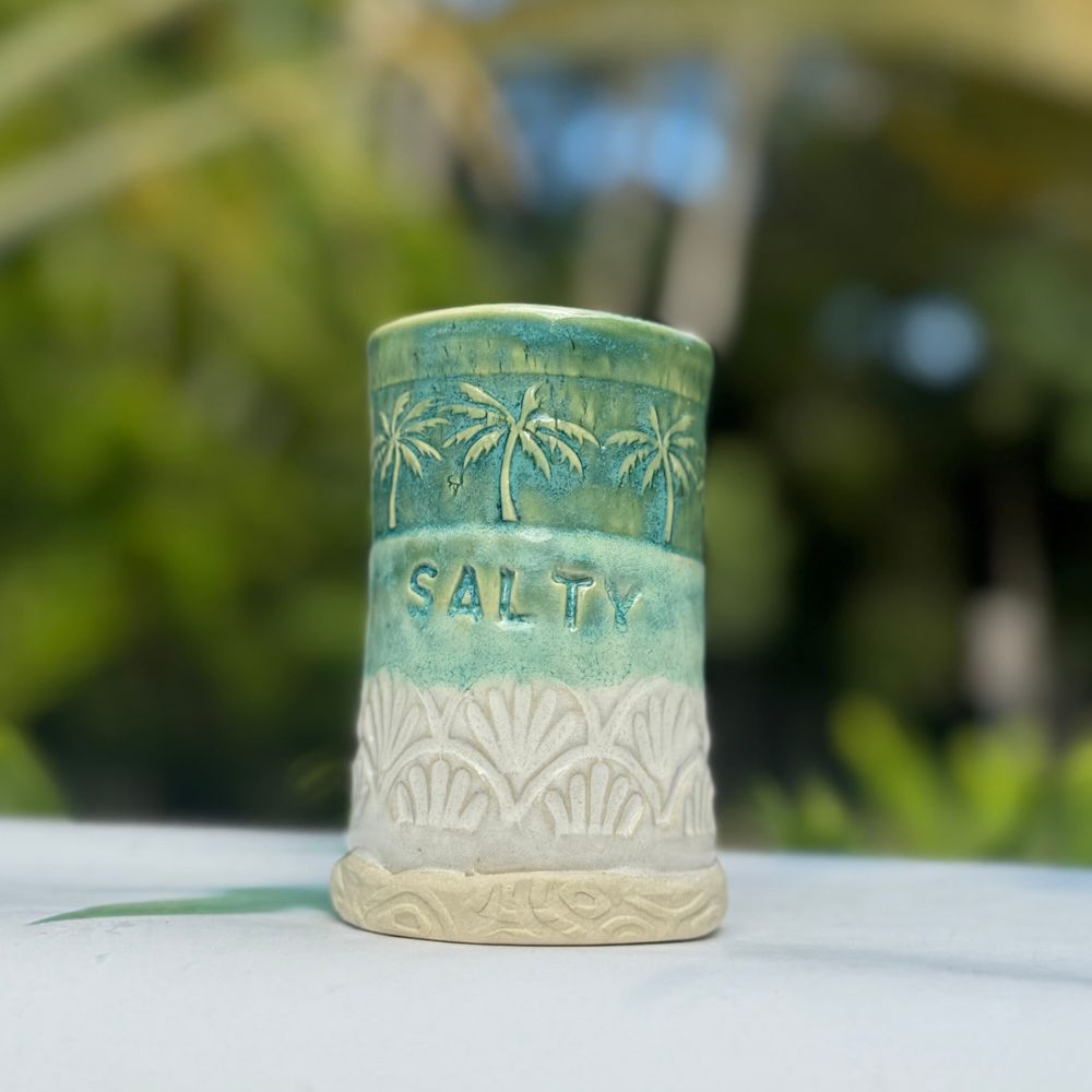 Ceramic container with 'Salty' text and palm tree design on a blurred natural background