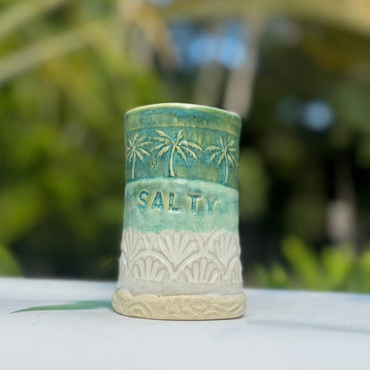 Ceramic container with 'Salty' text and palm tree design on a blurred natural background