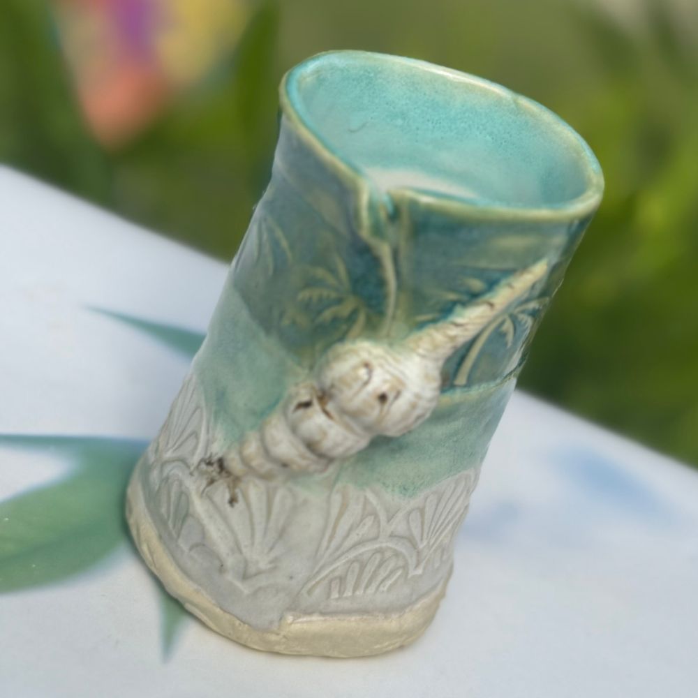 Ceramic vase with green and beige design on a blurred natural background