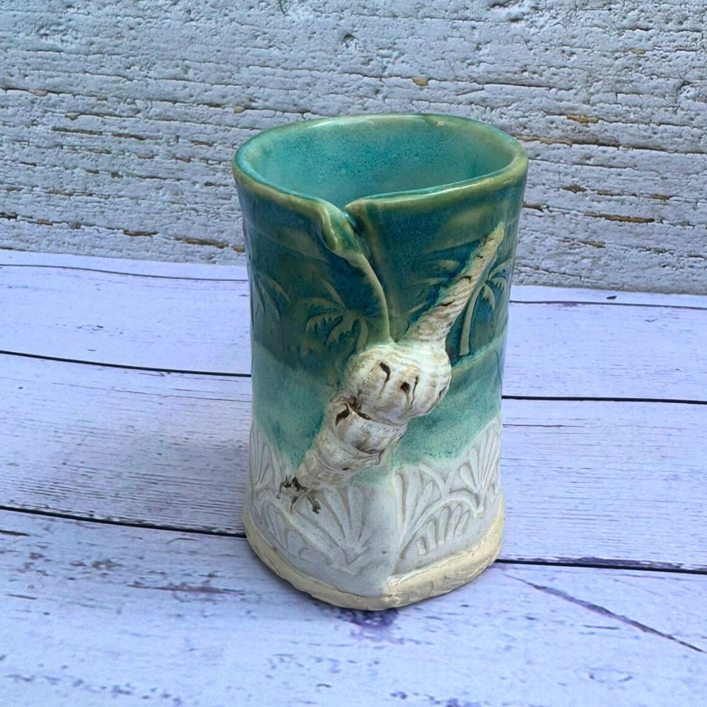Ceramic vase with a design of a palm tree and shells on a wooden surface