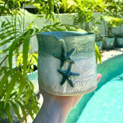 Ceramic planter with starfish design held in front of green foliage