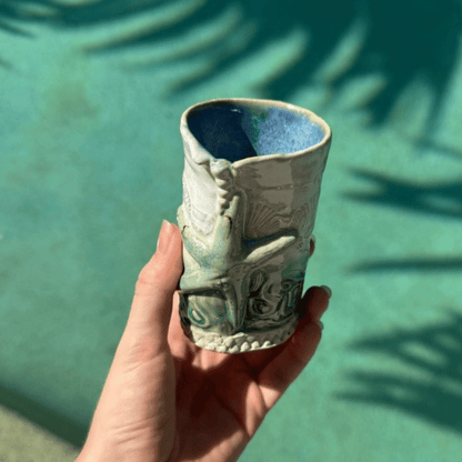 Hand holding a ceramic bud vase with a textured design against a green background