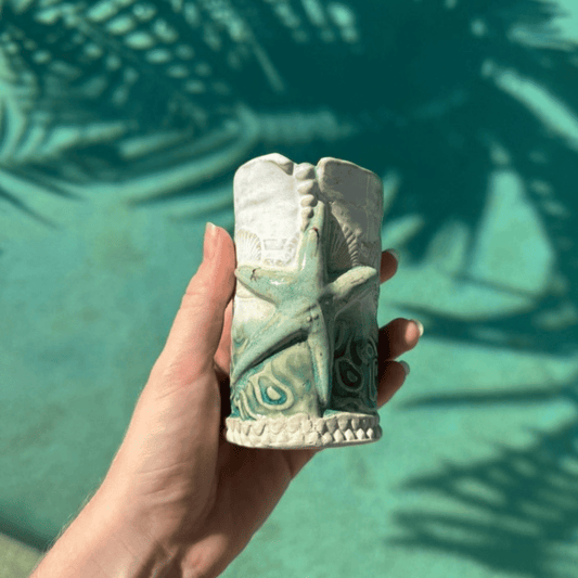 Hand holding a decorative ceramic bud vase against a teal background