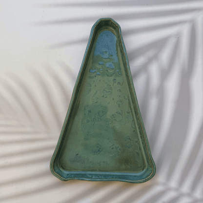 Triangular green ceramic dish on a textured white surface