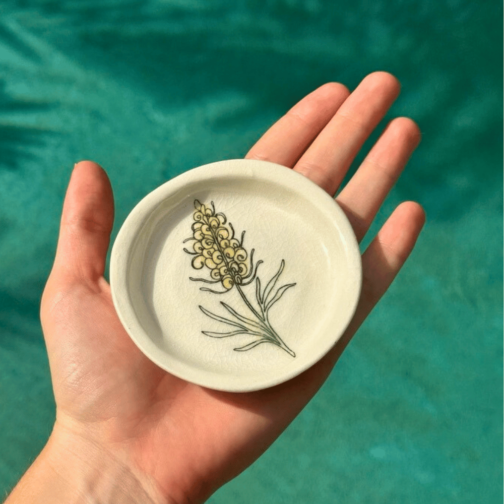 Hand holding a small ceramic dish with a floral design against a teal background