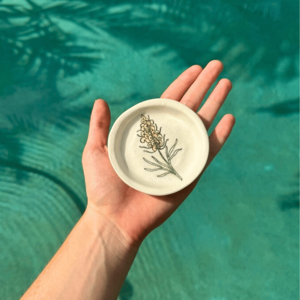 Hand holding a small ceramic plate with floral design against a teal water background