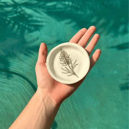 Hand holding a small ceramic plate with floral design against a teal water background