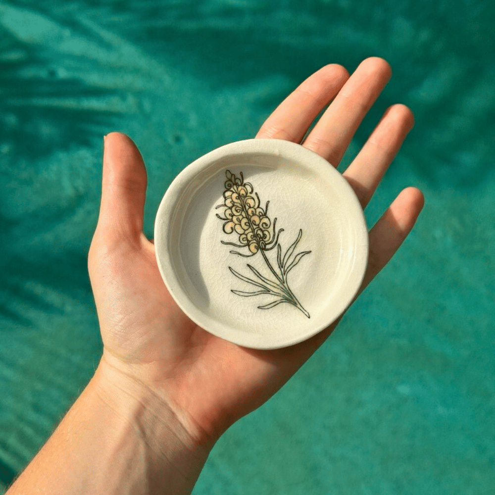 Hand holding a small ceramic dish with floral design against a teal background