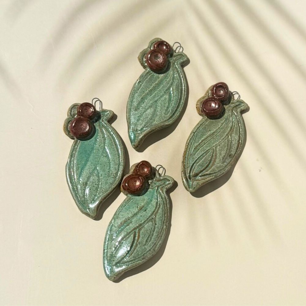 Set of three green ceramic leaf-shaped ornaments with brown berries on a beige background