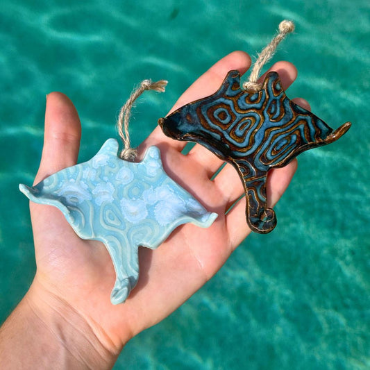 Two stingray-shaped ornaments held in a hand with a turquoise water background