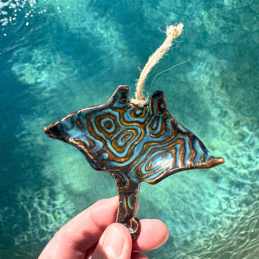 Decorative stingray ornament with wavy pattern held over clear blue water