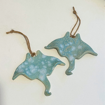 Two ceramic stingray-shaped ornaments with textured surfaces and string attachments on a light background.