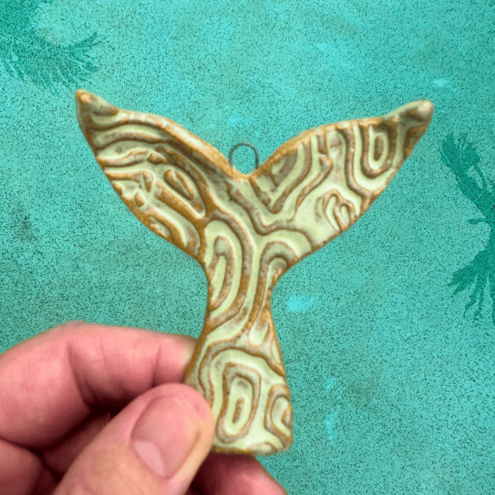 Decorative ceramic whale tail ornament held by a hand against a teal background