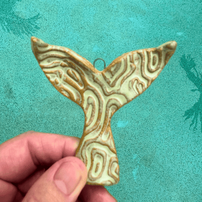 Decorative ceramic whale tail ornament held by a hand against a teal background