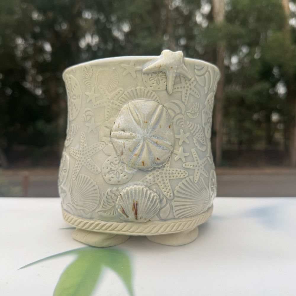 Ceramic pot with shell and starfish designs on a blurred natural background