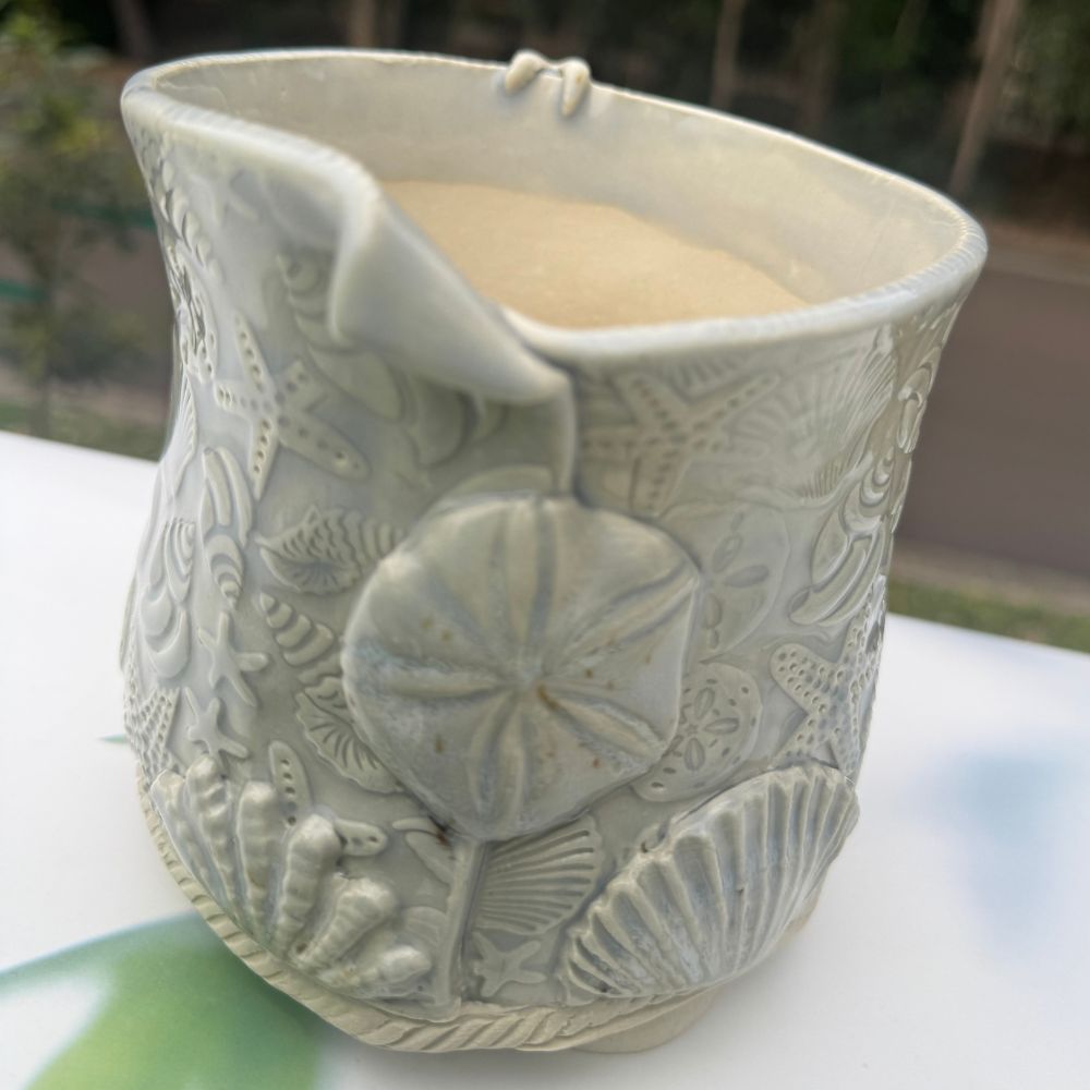 Ceramic planter with sand dollar and shell patterns on a white surface