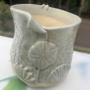 Ceramic planter with sand dollar and shell patterns on a white surface