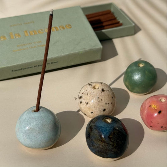 Colorful ceramic incense holders with incense sticks on a light surface.
