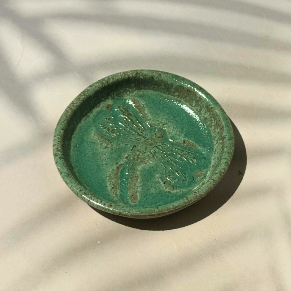 Green ceramic ring dish with a dragonfly design on a textured beige surface. Sunshine Pot-Tree, Sunshine Coast, Qld.