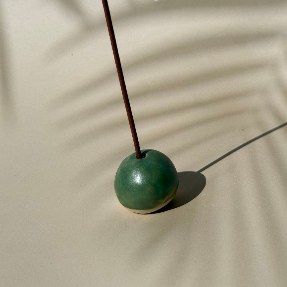 Green incense holder with a single incense stick on a beige surface